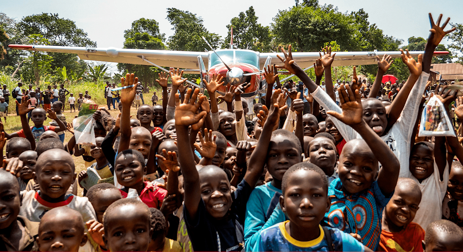 Large crowd of children in front of a small airplane